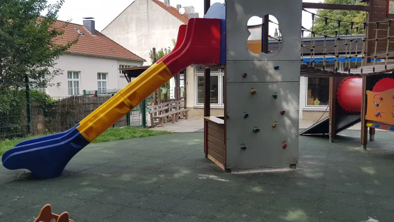 WARCO fall protection puzzle mats in the color grass green were laid under the play tower with slide, climbing wall and suspension bridge at a public children's playground.