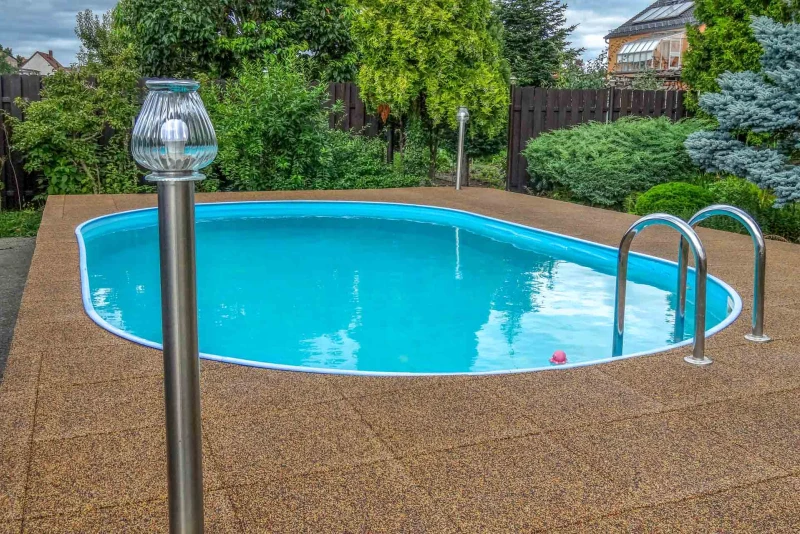 Der farblich in natürlichen  Erdtönen gehalten Umgang aus wasserdurchlässigen Schwimmbad-Fliesen (Farbdesign Terra Cotta)  passt hervorragend in die Gartenlandschaft, in der das Schwimmbecken steht. Gemauerter Pool mit braunem Belag und Leiter