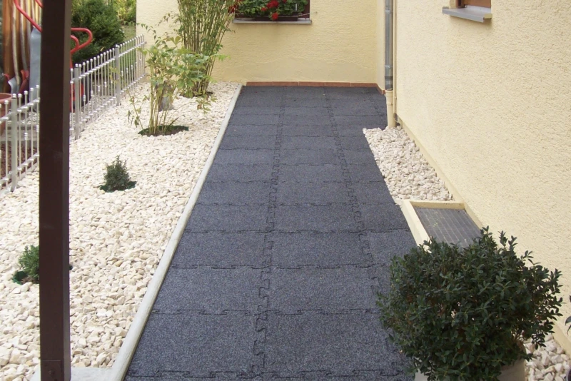 Rutsch hemmende und wetterfeste Gehwegplatten aus Gummigranulat liegen auf dem Weg durch den Garten zum seitlich am Haus liegenden Hauseingang.